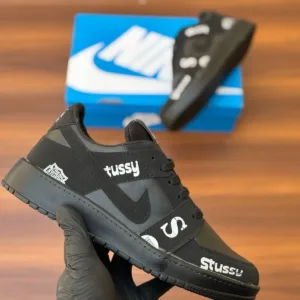 Budget-friendly streetwear sneakers with teal panels, cream swoop logo, yellow sole, and bold graphic patches, held in hand over a wooden background
