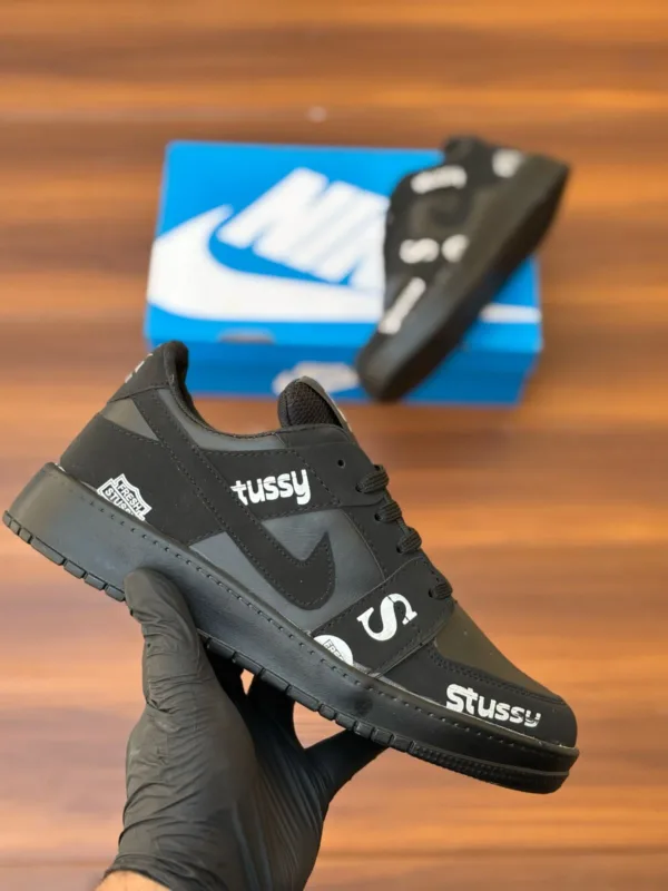 Budget-friendly streetwear sneakers with teal panels, cream swoop logo, yellow sole, and bold graphic patches, held in hand over a wooden background