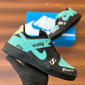 Budget-friendly streetwear sneakers with teal panels, cream swoop logo, yellow sole, and bold graphic patches, held in hand over a wooden background