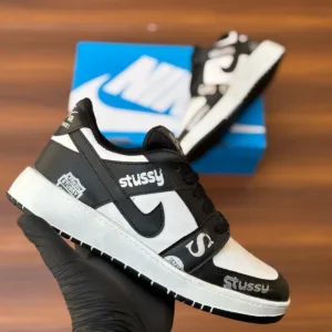 Budget-friendly streetwear sneakers with teal panels, cream swoop logo, yellow sole, and bold graphic patches, held in hand over a wooden background