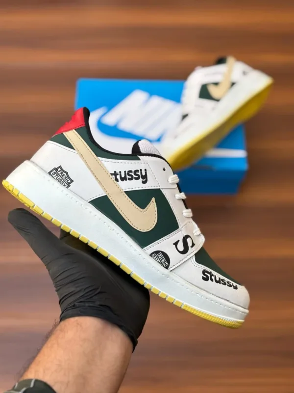 Budget-friendly streetwear sneakers with teal panels, cream swoop logo, yellow sole, and bold graphic patches, held in hand over a wooden background